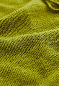 Zbliżenie na teksturowaną zieloną dzianinę, ukazujące szczegółowe szwy i miękkie fałdy.