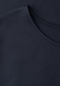 Gros plan d'un tissu bleu marine foncé avec une fine texture côtelée et une couture courbée, probablement une partie de l'encolure d'un vêtement.