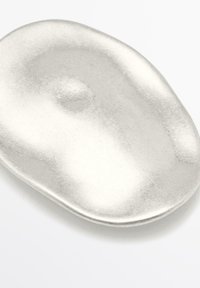 Metallisk silverfärgad serveringsskål med en jämn, oregelbunden, organisk form. Har en subtil textur och reflekterande yta.