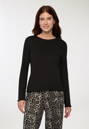 Maglietta nera a maniche lunghe con colletto rotondo e orlo sfrangiato, abbinata a pantaloni grigi e neri con stampa leopardata che presentano una vestibilità ampia.