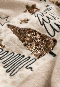 Tessuto beige con design di albero di Natale decorato con paillettes; comprende contorni neri e ulteriori motivi decorativi a forma di stella.