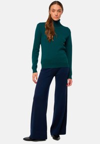 Türkisfarbener Rollkragensweater, kombiniert mit marineblauen weiten Beinkleidern. Der Sweater ist figurbetont und aus weichem Material; die Hosen sind locker und bodenlang mit einer glatten Textur.