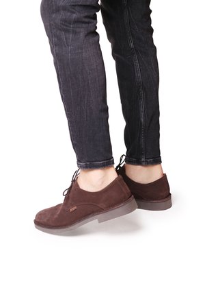 Scarpe in suede marrone con lacci, punta rotonda, suola in gomma piatta e texture morbida, abbinate a jeans scuri.