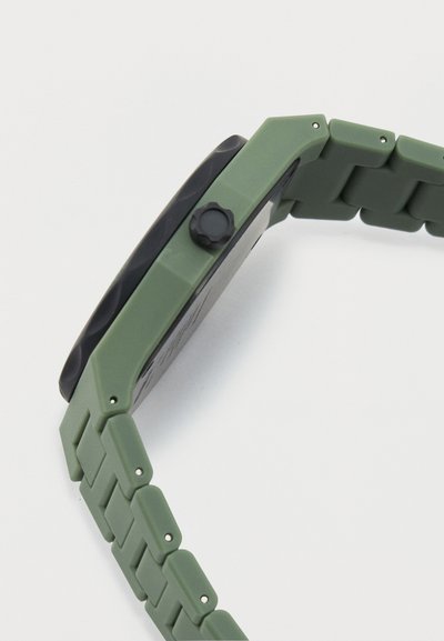 Πράσινο πλαστικό ρολόι χειρός με μαύρο καντράν και υφασμένο κορόνα, εμφανιζόμενο από πλάγια γωνία σε λευκό φόντο.