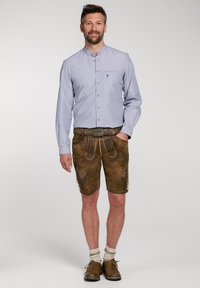 Ljusblå skjorta med knappar och bröstficka, kombinerad med bruna kortbyxor i läder, med dekorativ sömnad och knappdetaljer.