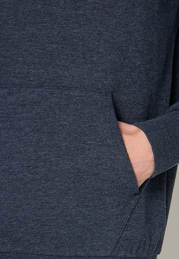 Main dans la poche avant d'un sweat-shirt ou d'un hoodie à manches longues texturé de couleur bleu foncé.