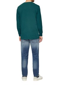Langsleeve teal shirt, katoenmix, ronde hals, gecombineerd met vervaagde blauwe jeans, slim fit, en witte sneakers. Heeft een casual ontwerp en eenvoud.