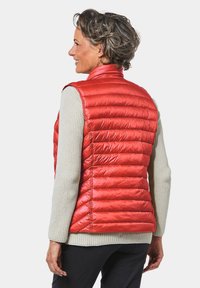 Rode geïsoleerde vest met een slim fit, voorzien van een doorgestikte patroon en hoge kraag, gedragen over een lichtgrijze trui, gecombineerd met donkere broek.