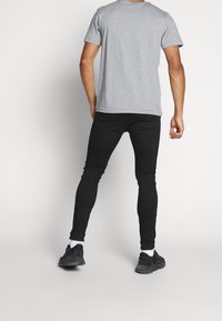 Camiseta de algodón gris combinada con jeans ajustados negros, vista desde la parte de atrás. Las zapatillas son negras con detalles blancos, mostrando un look casual.