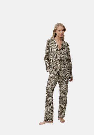 Donna in piedi a piedi nudi che indossa un completo pigiama coordinato con stampa zebrata con maniche lunghe e pantaloni su sfondo uniforme.