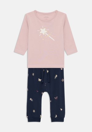 Rosa Langarmoberteil mit einem glitzernden Stern-Graphic, kombiniert mit marineblauen Hosen, die farbenfrohe Blumen- und Schmetterlingsmuster aufweisen. Elastischer Taillenbund.