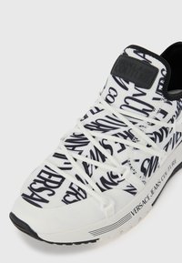 Versace Jeans Couture sneakers i hvit med svarte logoer, med en strukturert design, snøring og teksturert såle.