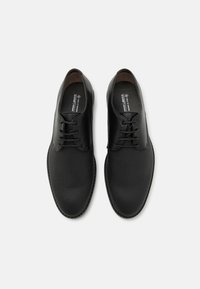 Black leather shoes with a smooth finish, rounded toe, lace-up design, and subtle texture. Interior branding visible on insoles.