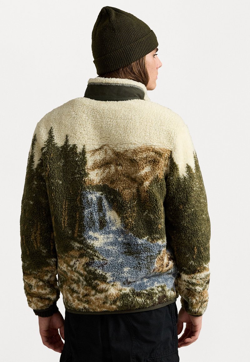 Sherpa-jacka med en naturscen med träd och ett vattenfall; främst i cream, grön och brun färg; textil med struktur och fluffig textur.