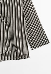Black and white striped garment with a loose fit, featuring a button closure, drop shoulders, and wide sleeves. Textured fabric.