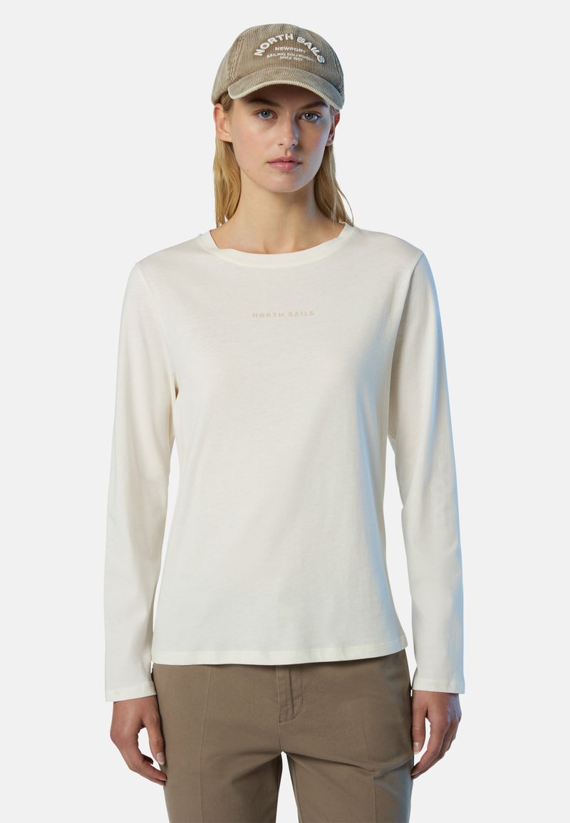 Camicia a maniche lunghe di colore crema con scollo rotondo e sottile stampa "NORTH SAILS" in una tonalità più chiara. Abbinata a berretto e pantaloni beige.
