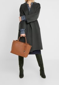 Brązowa torba tote o teksturowanej powierzchni z złotymi akcentami i zawieszką. Torba posiada wytrzymałe uchwyty oraz sztywną konstrukcję.