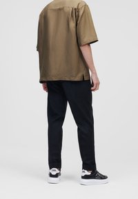 Olijf groene shirt met korte mouwen, ontspannen pasvorm, gecombineerd met zwarte broek en zwarte sneakers met witte zolen en logo. Op maat ontworpen, zonder patronen.