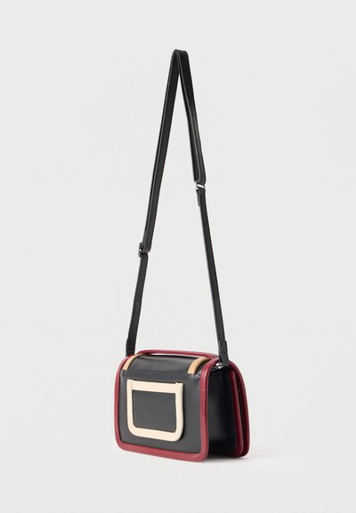 Μικρή ορθογώνια τσάντα ώμου με μαύρο σώμα, κόκκινο περίγραμμα, μπεζ πλαϊνά χειρολαβής και ρυθμιζόμενο μαύρο λουρί, κρεμασμένη σε λευκό φόντο.