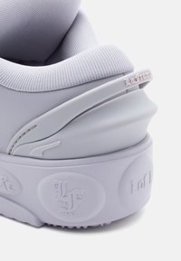 Detailní záběr na světle fialovou patu tenisky s texturovanou pěnovou podrážkou, polstrovaným síťovaným límcem a vyraženým logem "LF" a textem "La Femme".