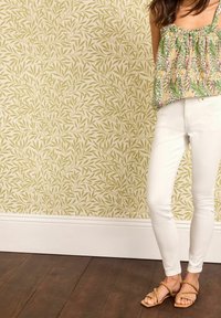 Hvide skinny jeans kombineret med en grøn mønstret peplum-top med blomsterdesign i gult og rødt. Brune sandaler fuldender looket.