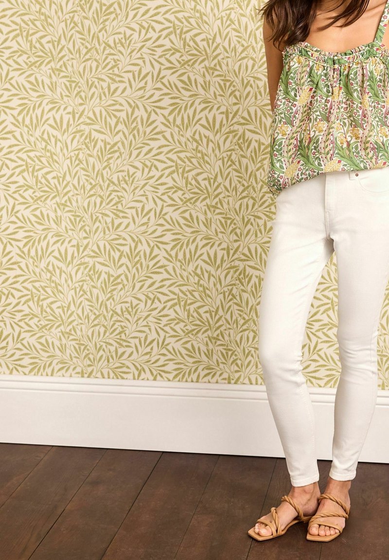 Hvide skinny jeans kombineret med en grøn mønstret peplum-top med blomsterdesign i gult og rødt. Brune sandaler fuldender looket.