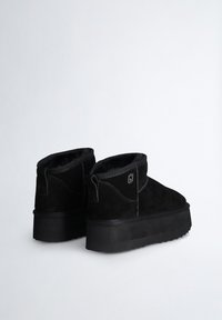 Stivaletti neri in suede con suola platform spessa nera, fodera in pelliccia e un tassello a ciclo sul retro per indossarli facilmente.