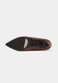 Ruskea nahkainen kenkä, jossa on kärjellinen varvas, tyylikäs yläosa ja musta kumipohja, johon on painettu logo ja joka on sileä pinta.