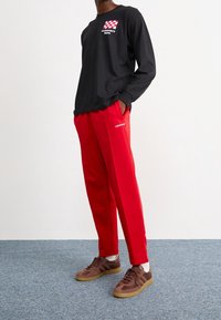 Svart långärmad tröja med röd och vit rutigt grafik. Röda träningsbyxor med vit logotyp. Bruna sportskor med gummisula.