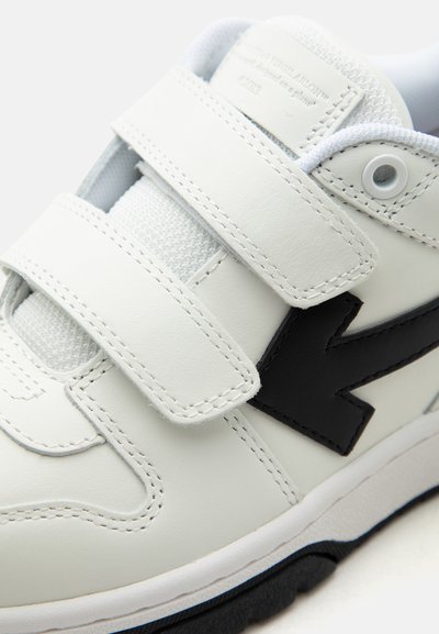 Άσπρο αθλητικό παπούτσι με δύο φαρδιές λουράκια βέλκρο και μαύρο σχέδιο σε σχήμα βέλους στο πλάι, με λευκά κορδόνια και υφασμένο πέλμα.