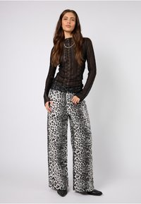 Schwarzes Langarmoberteil aus strukturiertem Stoff; kombiniert mit weitem Hosenbeinen mit schwarz-weißem Leopardenmuster; elegante schwarze Schuhe.