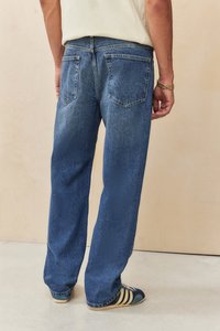 Blue denim jeans with a relaxed fit, featuring two back pockets and visible stitching. Worn with blue and gold athletic shoes.