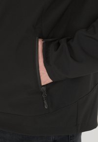 Black soft-shell jacket featuring a zippered side pocket, elastic cuffs, and a smooth, textured finish with minimal seams.
