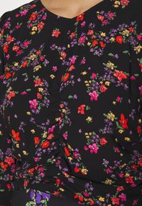 Tissu noir avec petit imprimé floral rouge, rose, violet et jaune, et subtil détail froncé sur l'encolure avant et la zone de la taille.