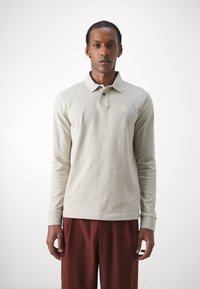 Lys beige langærmet polo skjorte med krave, to knapper og et lille logo mærke på brystet. Glat bomuldsstof.