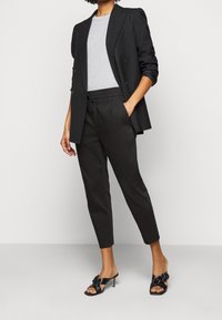 Svart dubbelknäppt kavaj över en grå t-shirt, kombinerad med svarta tapered byxor och svarta sandaler med slides som har en blommig accent.