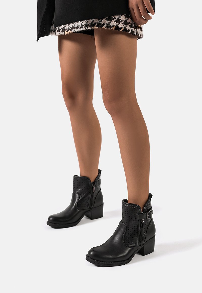 Stivaletti neri alla caviglia in pelle liscia con pannelli laterali testurizzati, chiusura con zip e tacco quadrato. Presentano sottili perforazioni e cinturini.