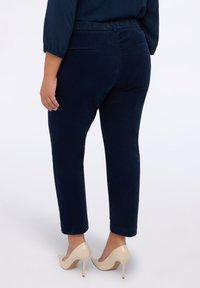 Granatowe spodnie z kordurowej tkaniny o slim fit, z elastycznym pasem i kieszeniami, zestawione z cielistymi szpilkami.