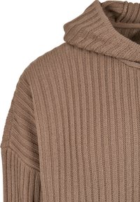 Pull en maille beige avec un col montant, présentant une texture côtelée et une coupe décontractée. Le tissu a des coutures visibles et une finition douce.