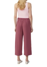 Pantalons cropped à jambes larges avec taille élastique, dans une couleur rose douce ; associés à un débardeur ajusté rose et des chaussures slip-on blanches perforées.