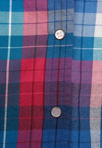 Plaid fabric in shades of blue, pink, and purple with a button at the center. Features a textured weave and contrasting color lines.
