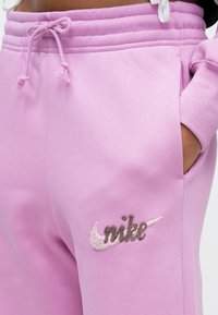 Ροζ παντελόνι φόρμας από μαλακό ύφασμα, με ελαστική μέση με κορδόνι και πλαϊνές τσέπες. Το λογότυπο της Nike είναι κεντημένο σε αντιθετικά χρώματα.