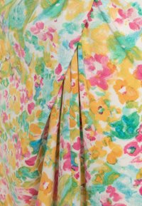 Tissu à motif floral avec des éclaboussures de couleurs rose, jaune et vert. Le matériau est doux, avec des détails plissés et une texture légère.