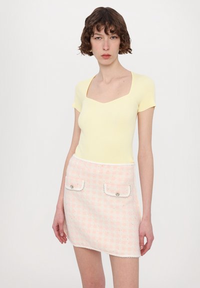 Kollane ribbed lühikeste varrukatega tops, millel on ruudukujuline kaelus; roosa ja valge tweed-seelik, millel on taskud ja dekoratiivsed nupud; tekstureeritud viimistlus.