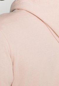 Sudadera rosa claro hecha de una tela suave, con un corte relajado y una capucha forrada. La superficie tiene una textura lisa con detalles de costura sutiles.