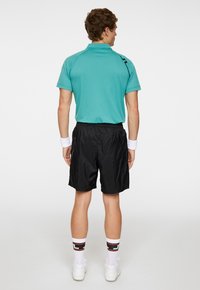 Herrarnas sportiga outfit med en teal polo t-shirt med svarta detaljer, svarta shorts och vita strumpor med färgglada mönster. Avslappnad sportkläddesign.