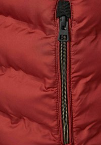Rote Daunenjacke mit einem zentralen schwarzen Reißverschluss mit goldenen Zähnen, glatter Textur und gestepptem Muster zur Isolierung.