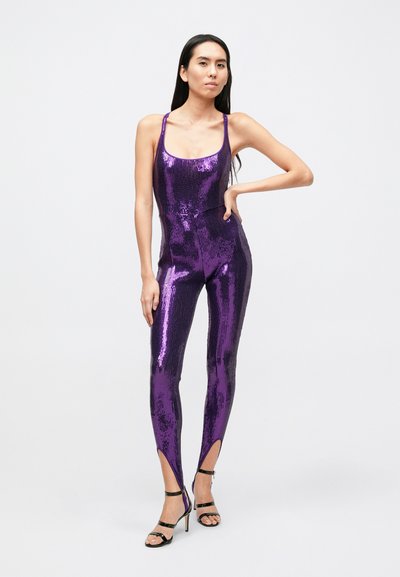Combinaison violette à sequins avec fines bretelles, coupe près du corps, fentes latérales aux chevilles, associée à des escarpins noirs à lanières.