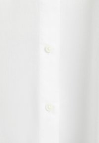 Camicia bianca realizzata in un tessuto leggero e morbido, con chiusura a bottoni e due bottoni tondi di colore chiaro.