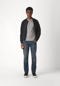 Ναυτική τζάκετ από βομβαρδιστικό πάνω από γκρι μπλούζα, συνδυασμένο με μπλε τζιν και μαύρα αθλητικά παπούτσια. Το τζάκετ έχει φερμουάρ μπροστά και ριμπ μανίκια.